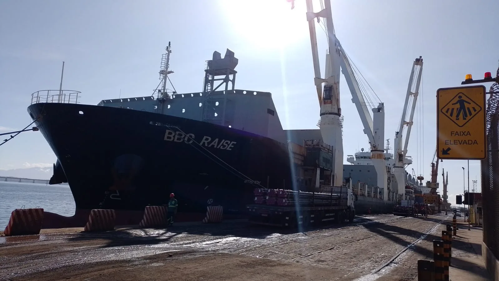 Break bulk vessel BBC Raise alongside a Brazilian port terminal, with ship cranes loading steel cargo from a truck